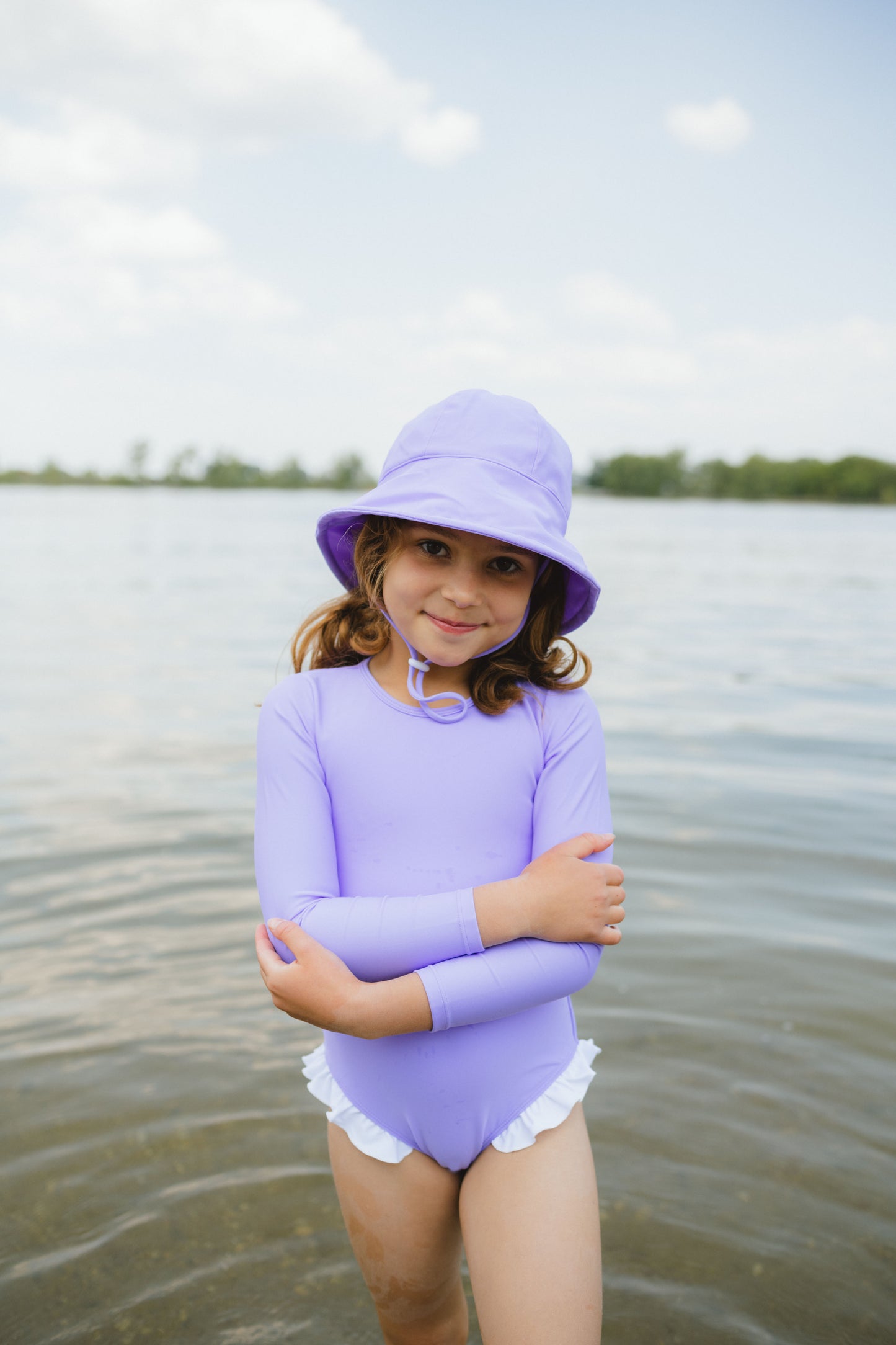 Young girl in a purple swimsuit and hat standing in water with a blurred background