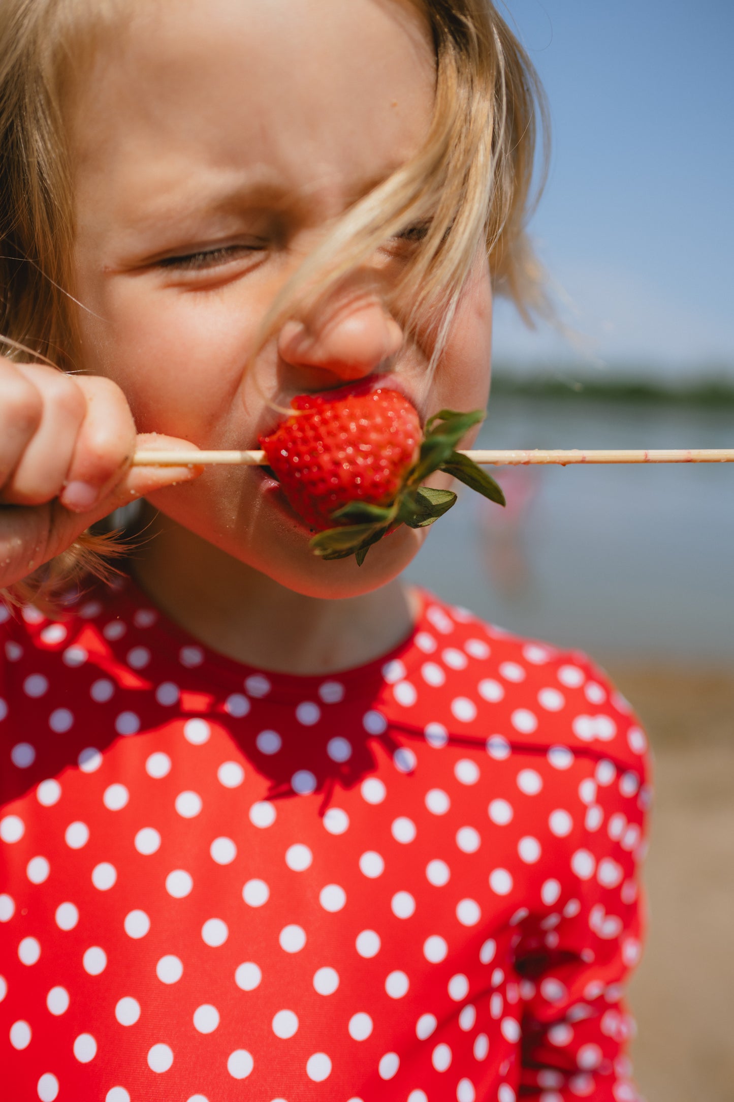 Child in red polka dot long sleeve swimsuit by the lake