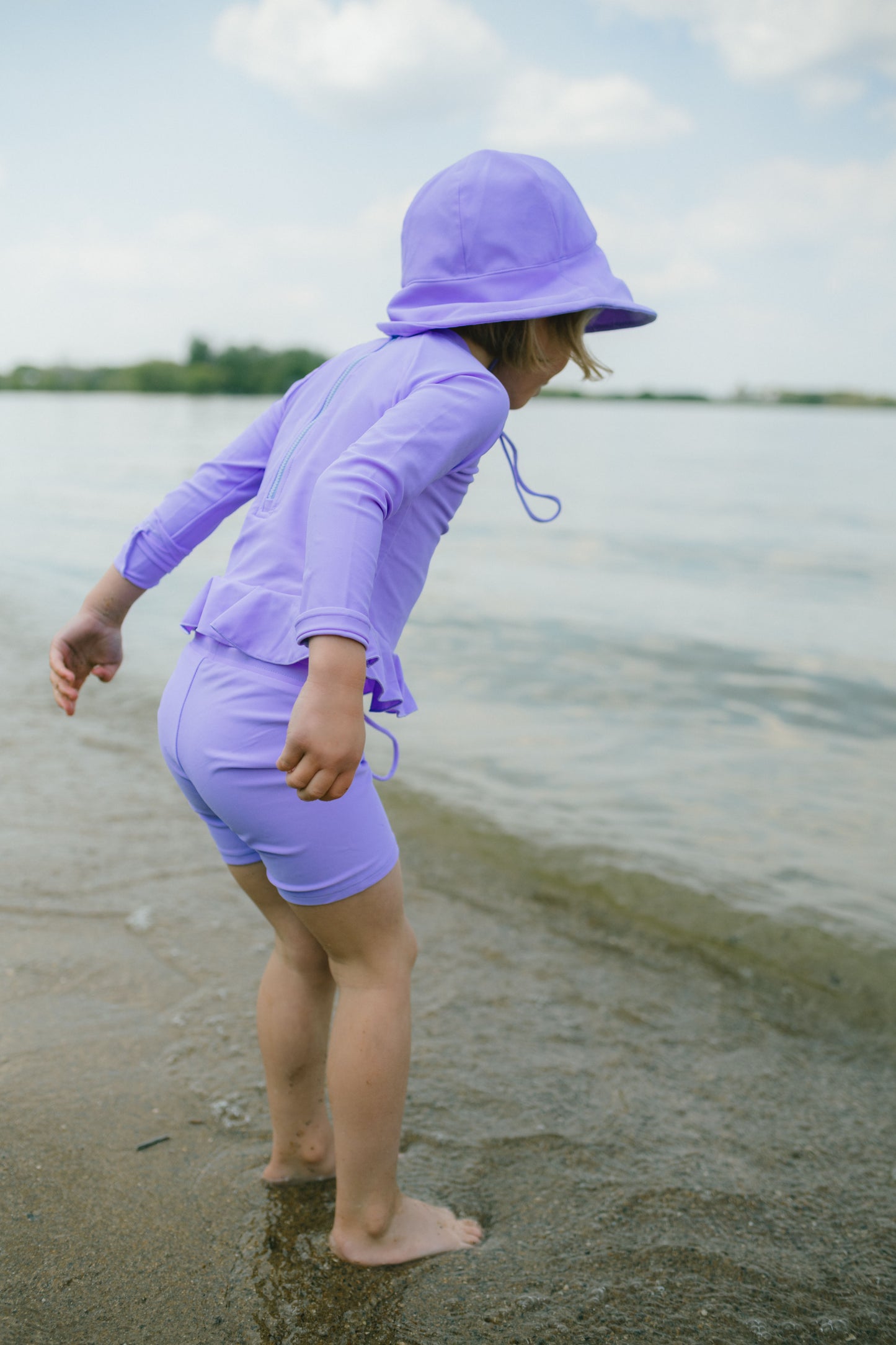 Child in purple sun protection outfit standing on a beach