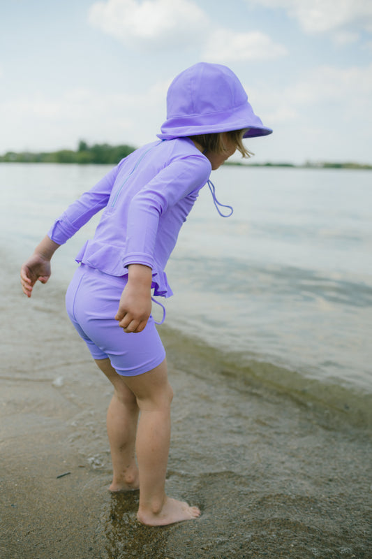 Child in purple sun protection outfit standing on a beach