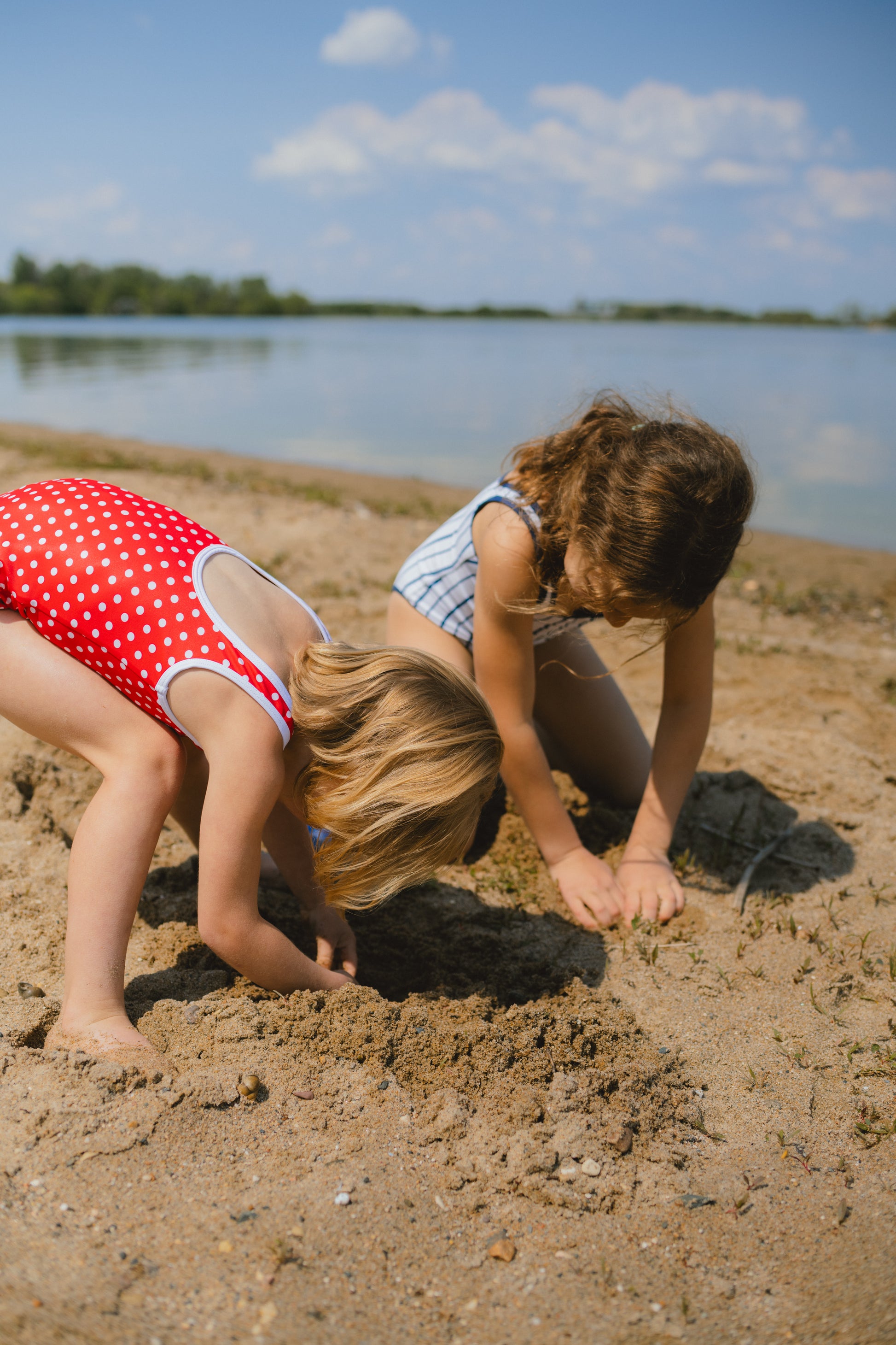 Two children playing in the sand by a lake on a sunny day.