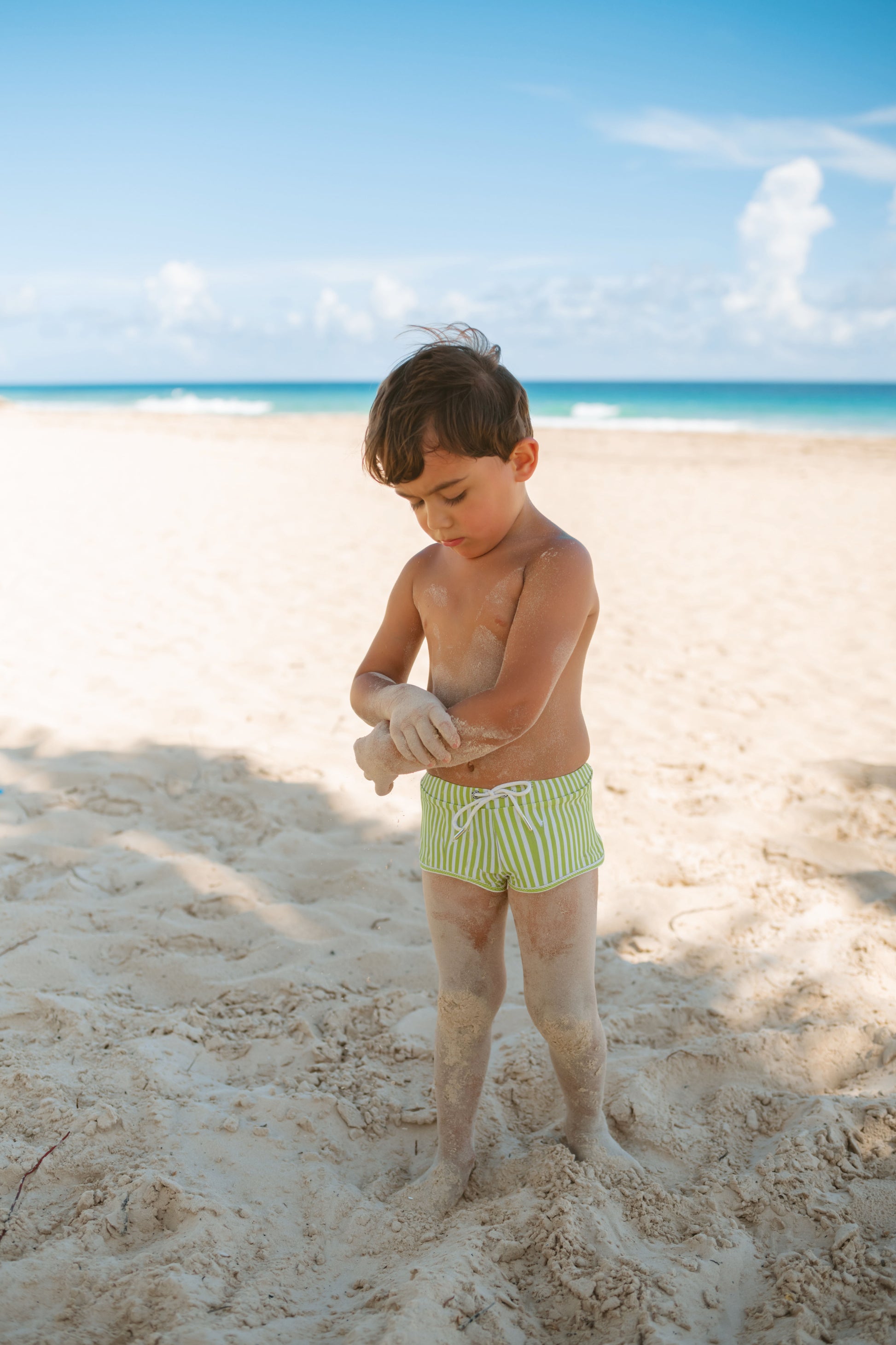 Child playing in the sand on a beach with blue sky and ocean in the background